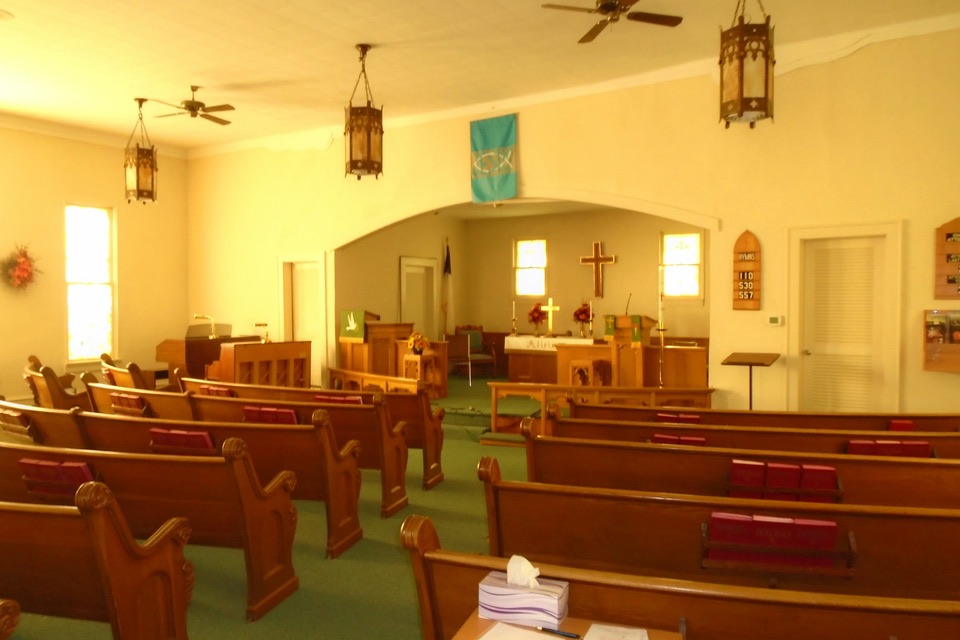 Wooden pews in a small, warmly lit church sanctuary with a cross at the front