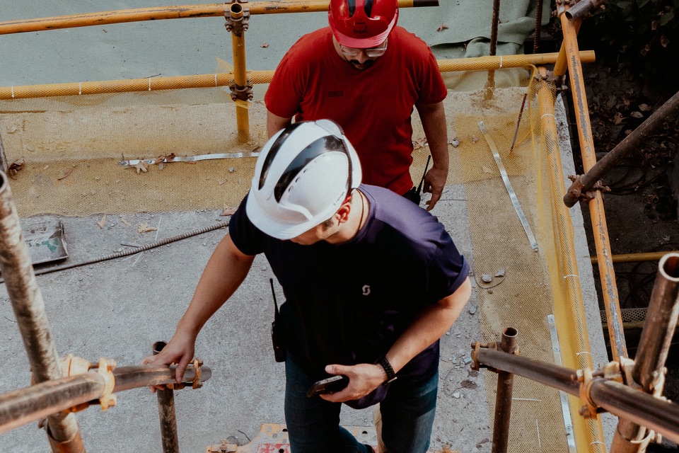 Two construction workers in hard hats climbing scaffold stairs on a building site