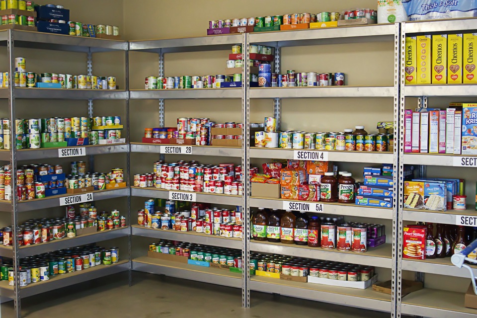 Food pantry shelves stocked with canned and boxed food, labeled by section