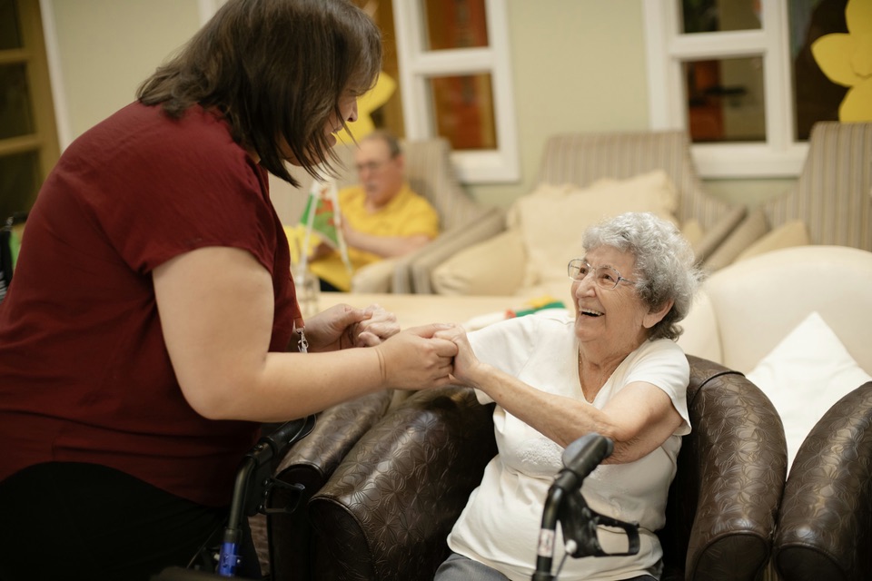 A caregiver holding hands with a smiling older woman who uses a walker