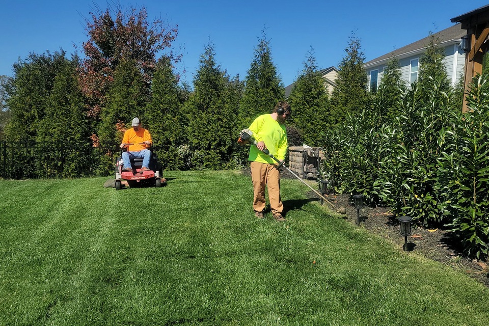 A two-person landscaping crew mowing and trimming a residential lawn