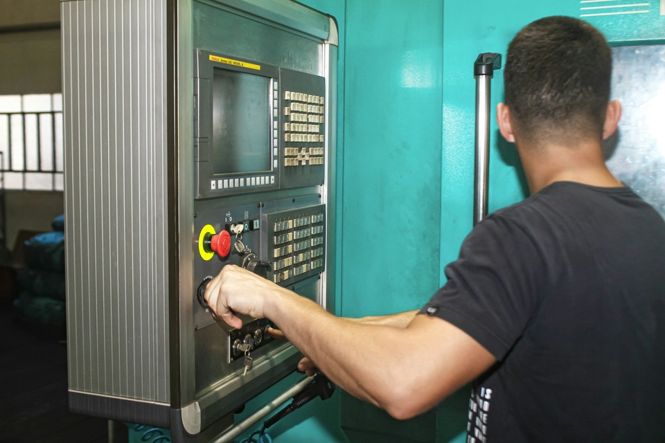 A machinist operating the control panel of a CNC machine in a shop