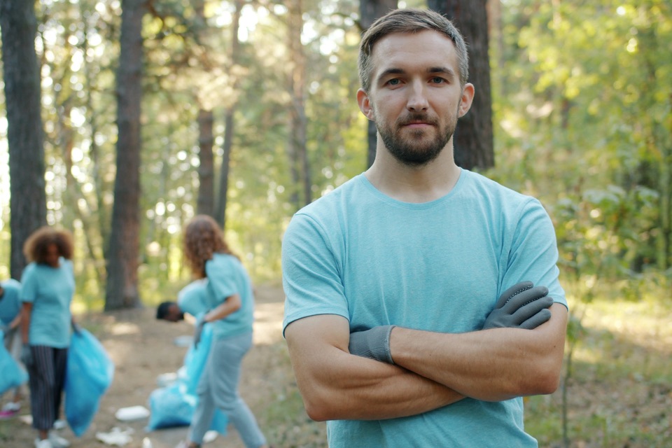 A volunteer in work gloves in front of a crew collecting litter in a wooded park