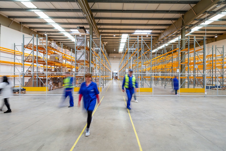 Workers in safety vests walking through a large warehouse during a shift