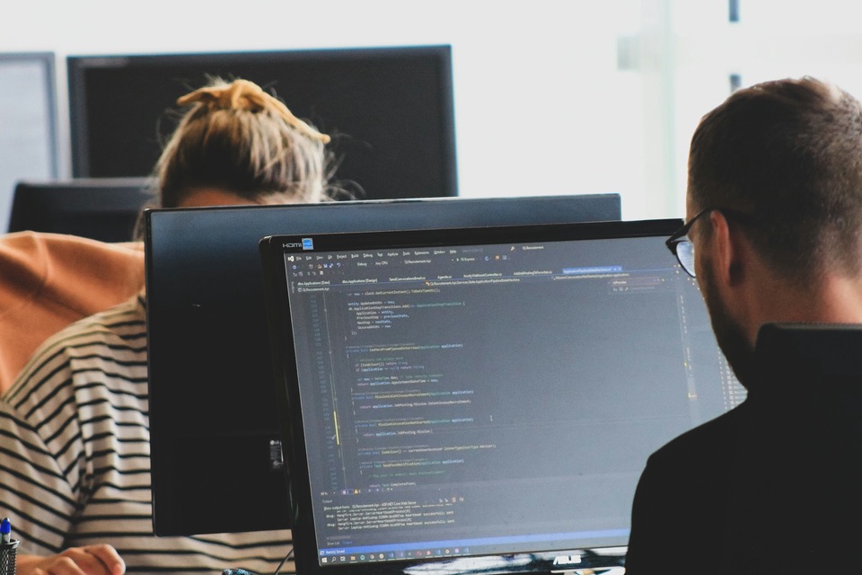 Two developers working on code at monitors in a shared office