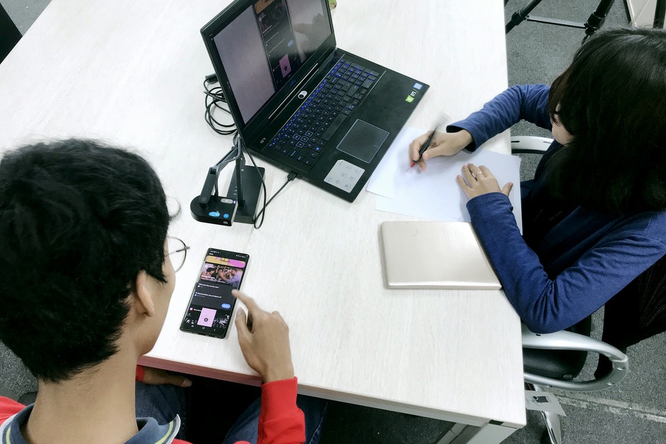 A usability test: one person tries an app on a phone while a researcher takes notes
